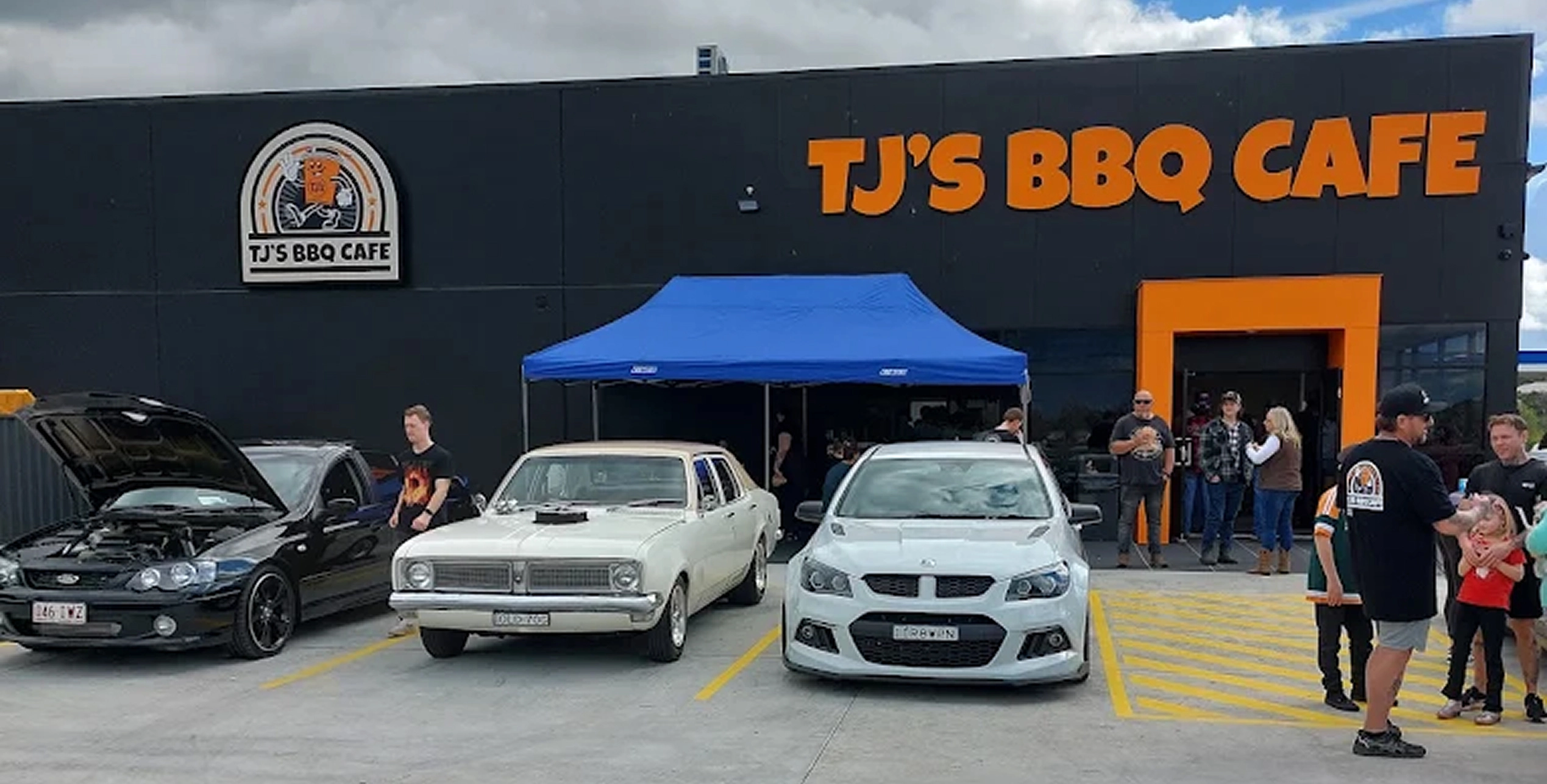 TJ's BBQ Cafe storefront and badge logo signage during a community car show event